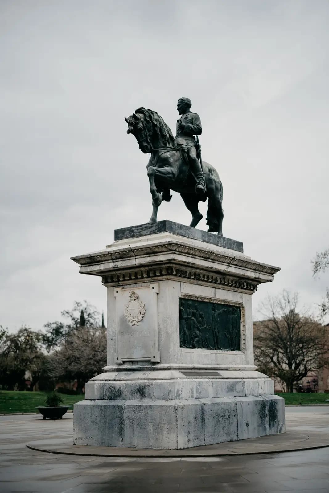 A bronze statue of a rider on horseback on a stone plinth in an empty paved square.