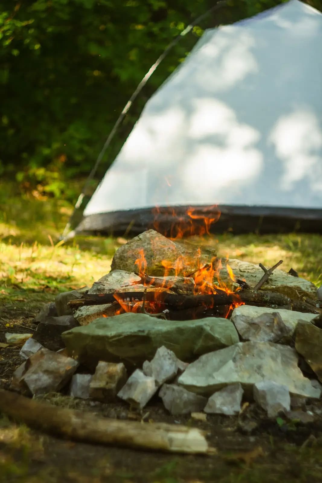 A stone fire ring beside a stack of firewood at a campsite.