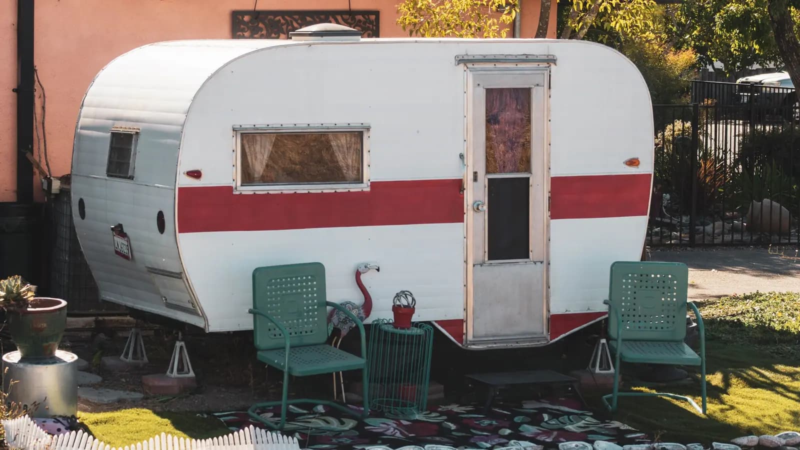 A vintage red-striped camper with green metal chairs out front.