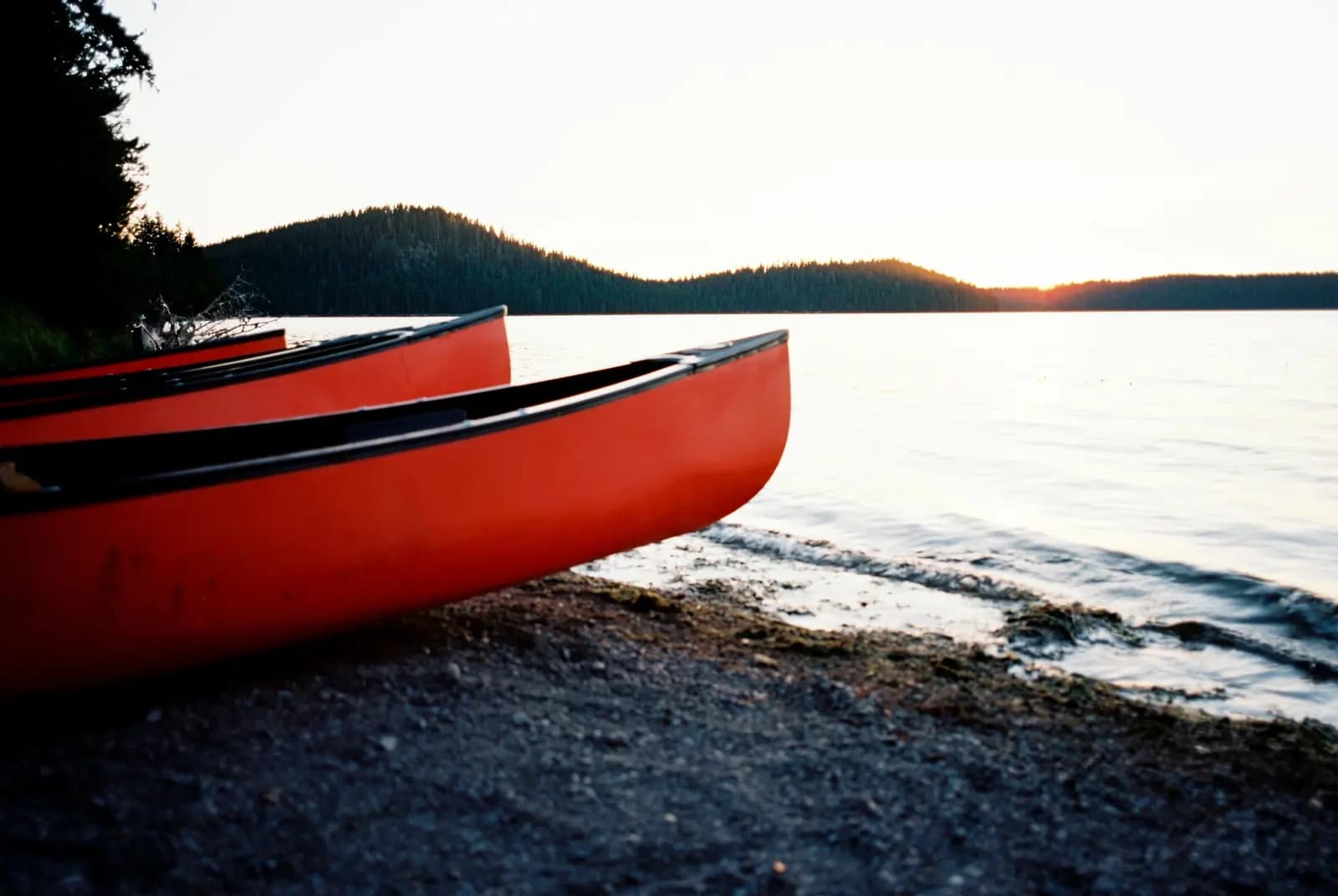 Two red canoes pulled up on a lakeshore at sunset.