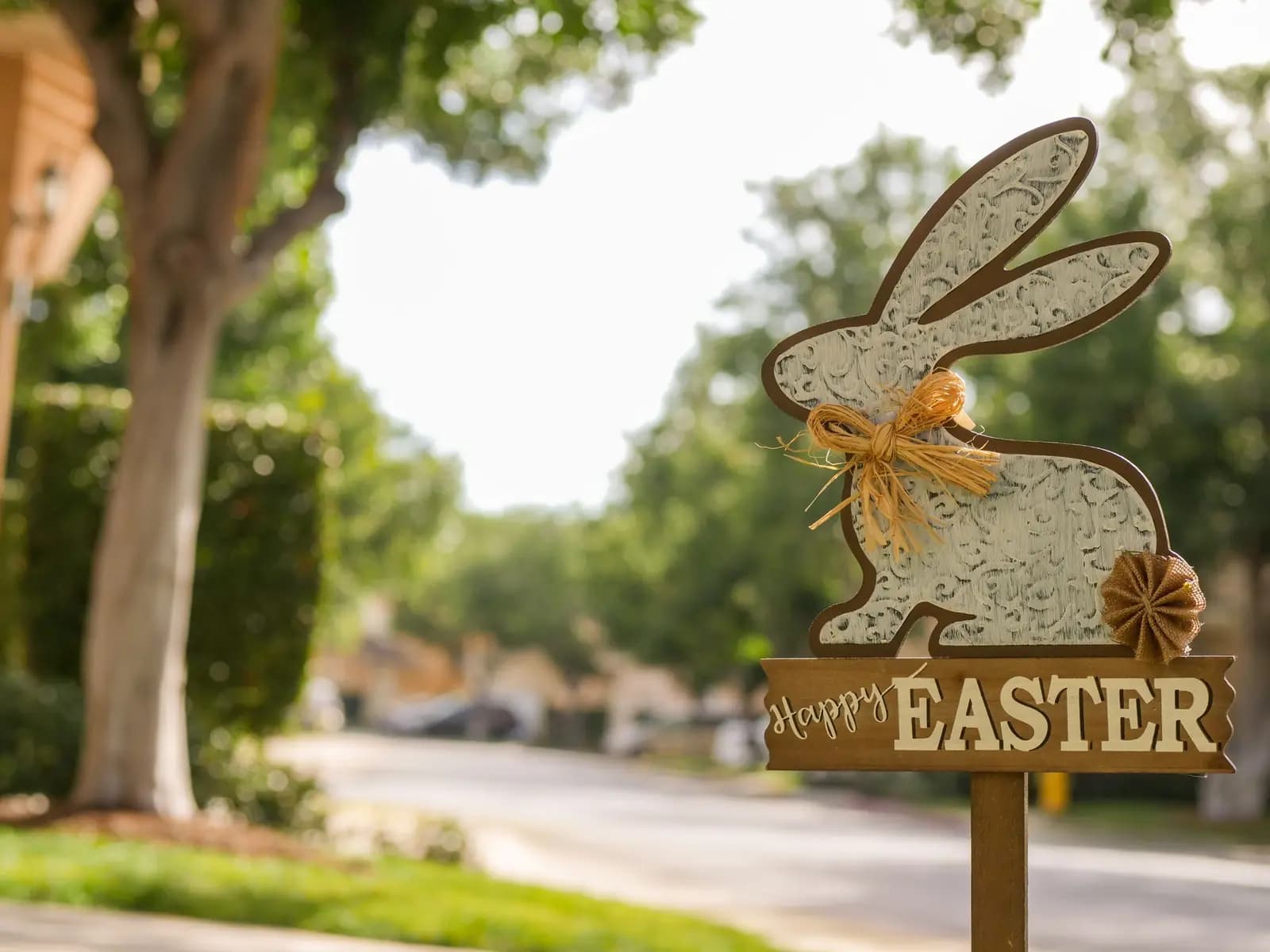 A Happy Easter bunny sign on a post beside a tree-lined suburban street.