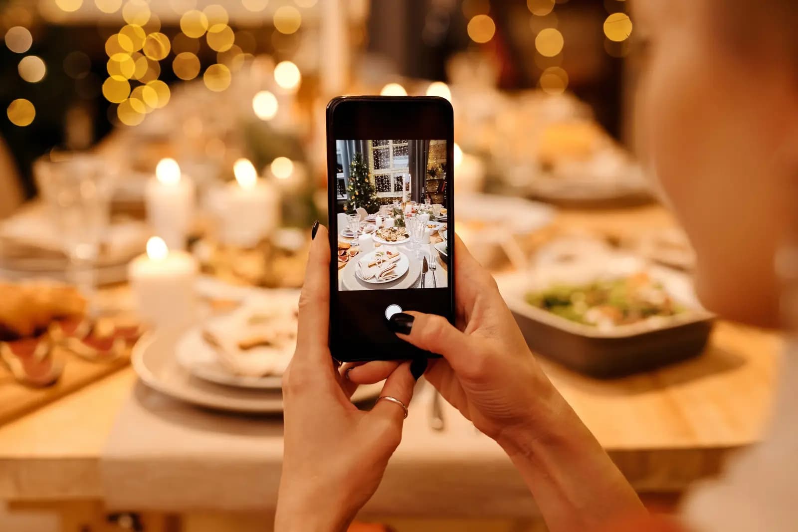 Hands hold a phone up over a candlelit dinner table, with the camera open.