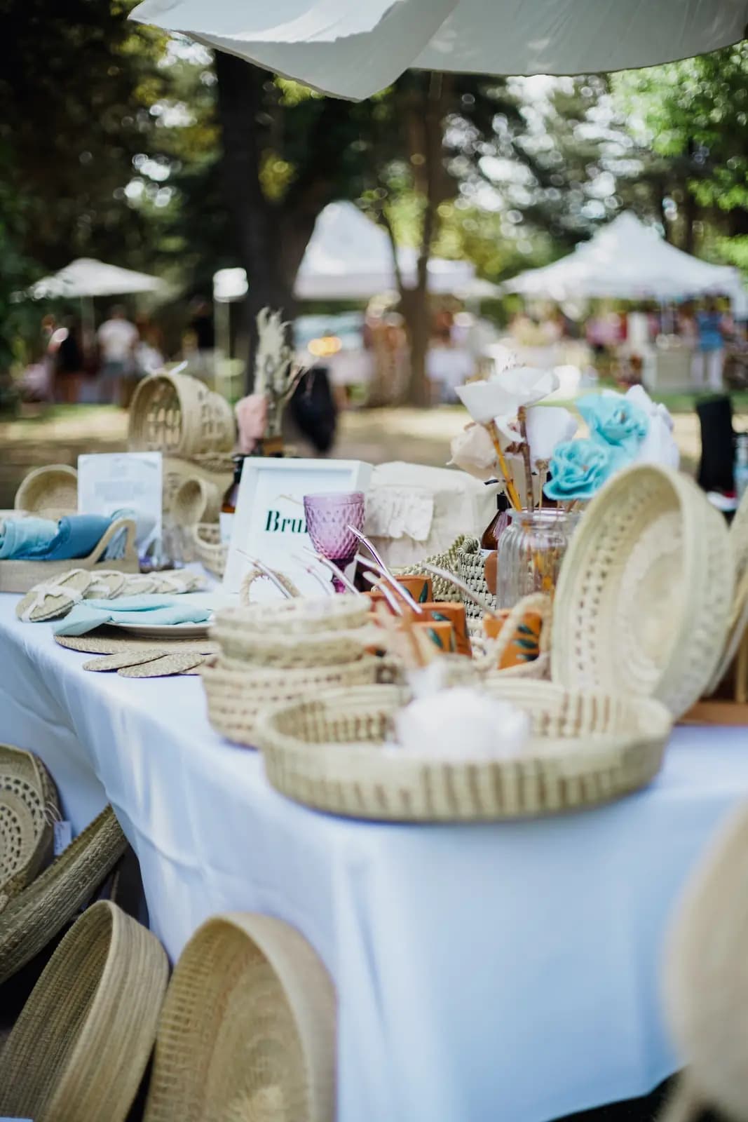 An outdoor table with a white cloth covered in woven baskets and small goods under a canopy.