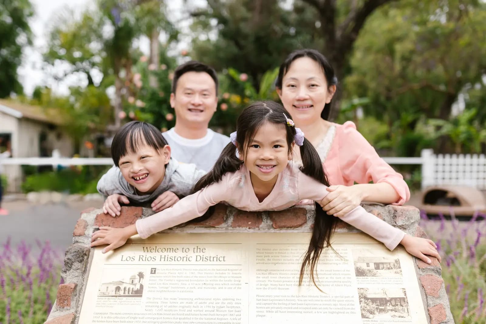 A mother, a father and two children lean over a historical marker in a small town, smiling at the camera.