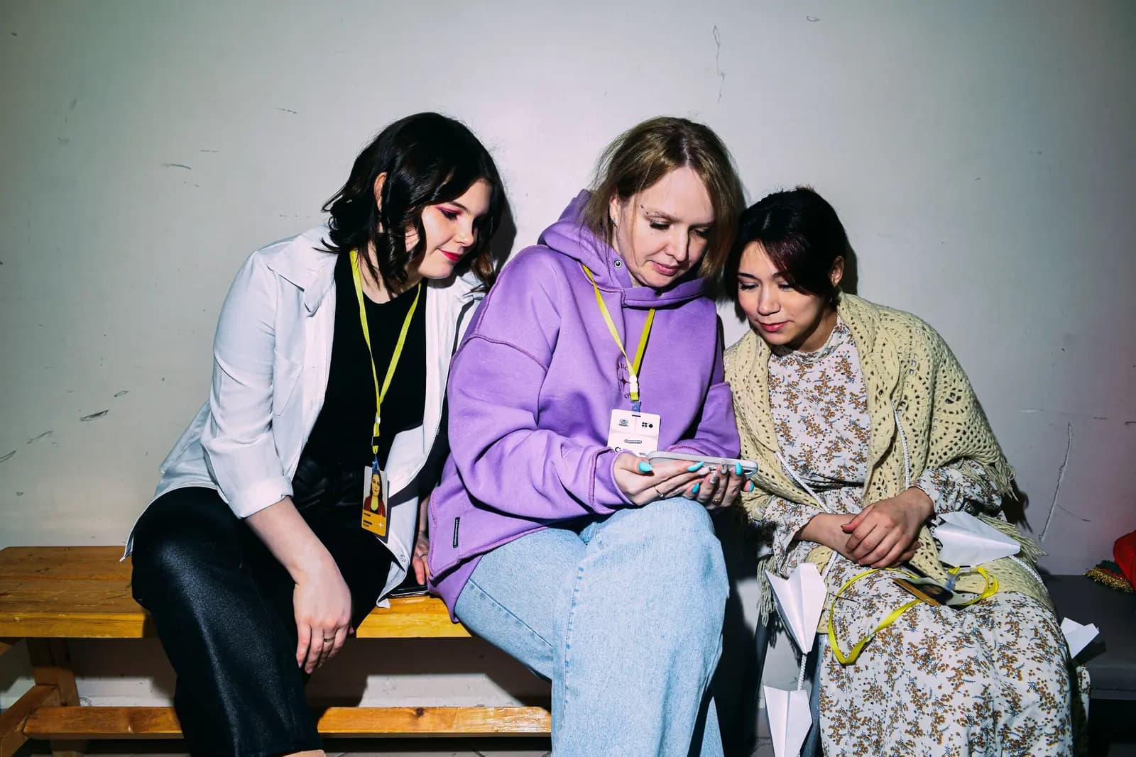 Three attendees with lanyards sit on a bench looking at one phone together.