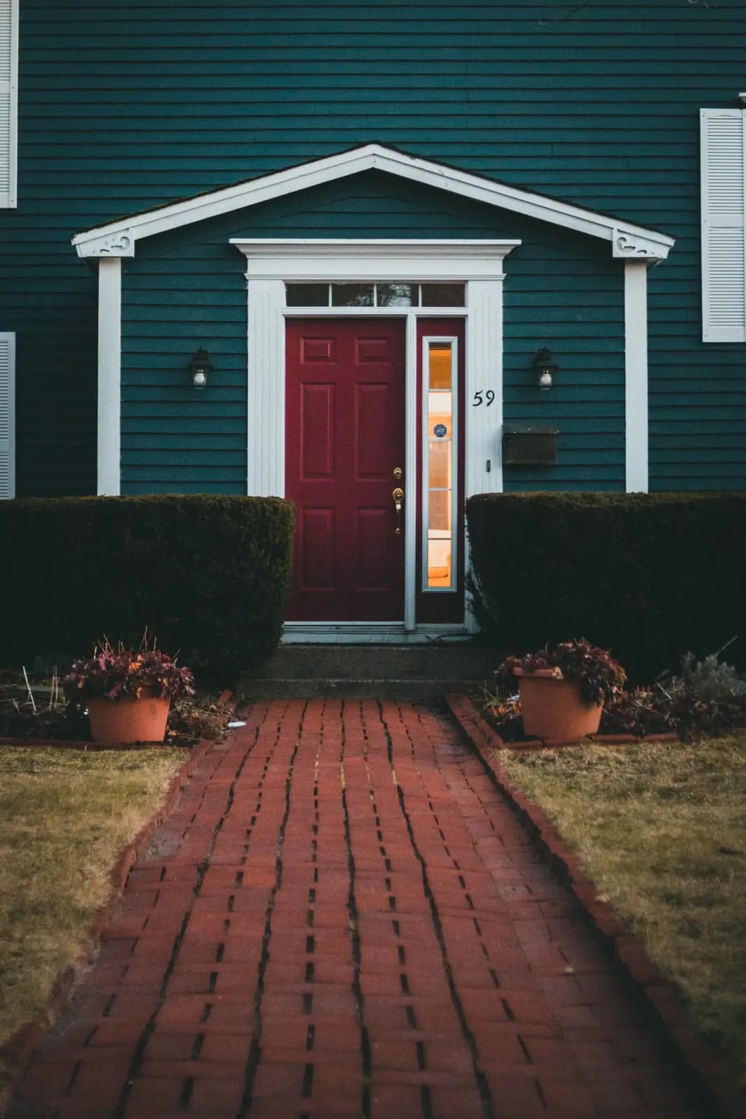 A red front door on a teal clapboard house at the end of a brick path.