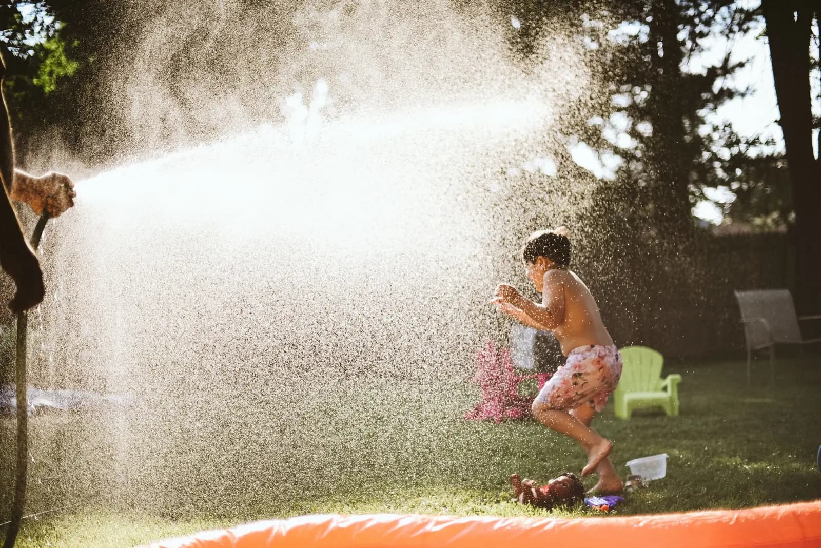 A boy jumps through spray from a hose in a sunny backyard.