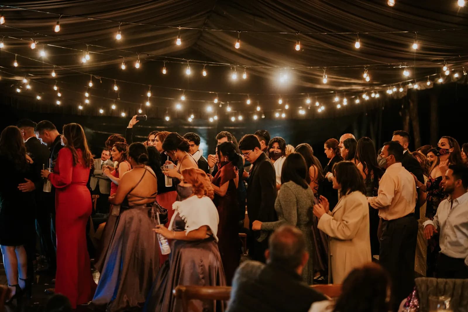Guests mingle at an evening wedding reception under a canopy of string lights.