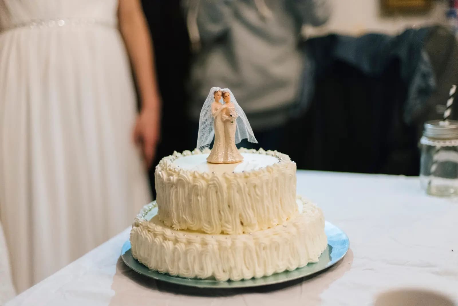 A two-tier wedding cake with a bride-and-groom topper on a reception table.