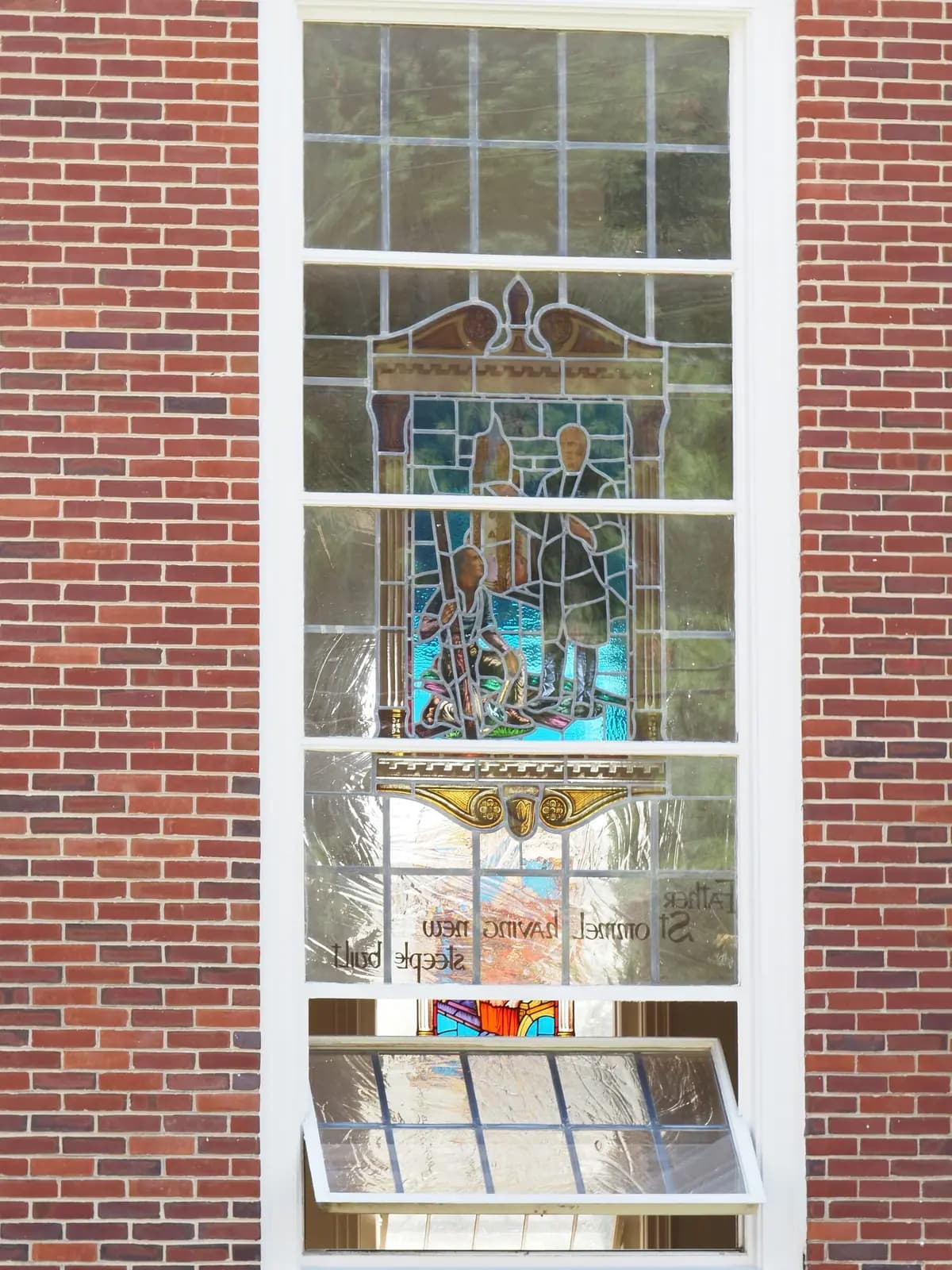 A stained glass window set in a red brick church wall.