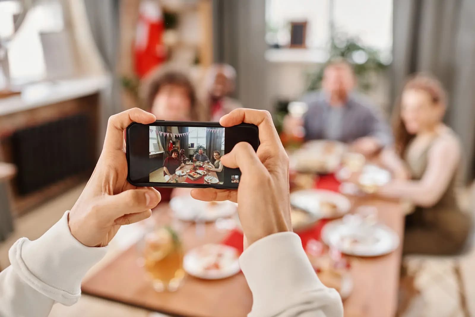 Hands frame a phone photo of a group of friends around a dinner table.