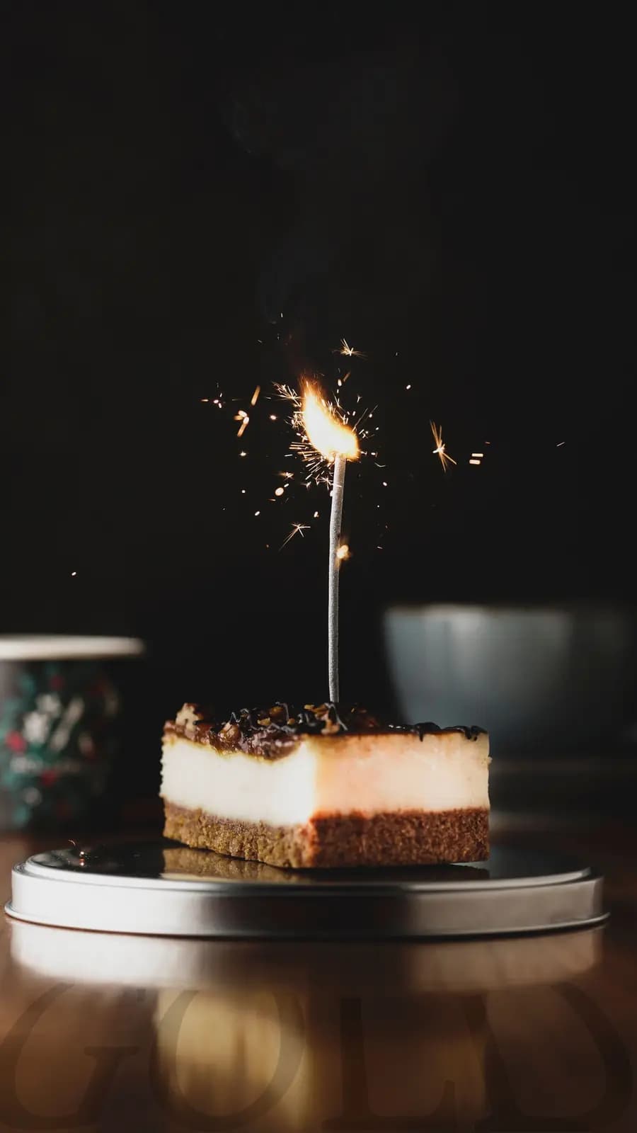 A sparkler burning on a slice of cheesecake on a dark table.