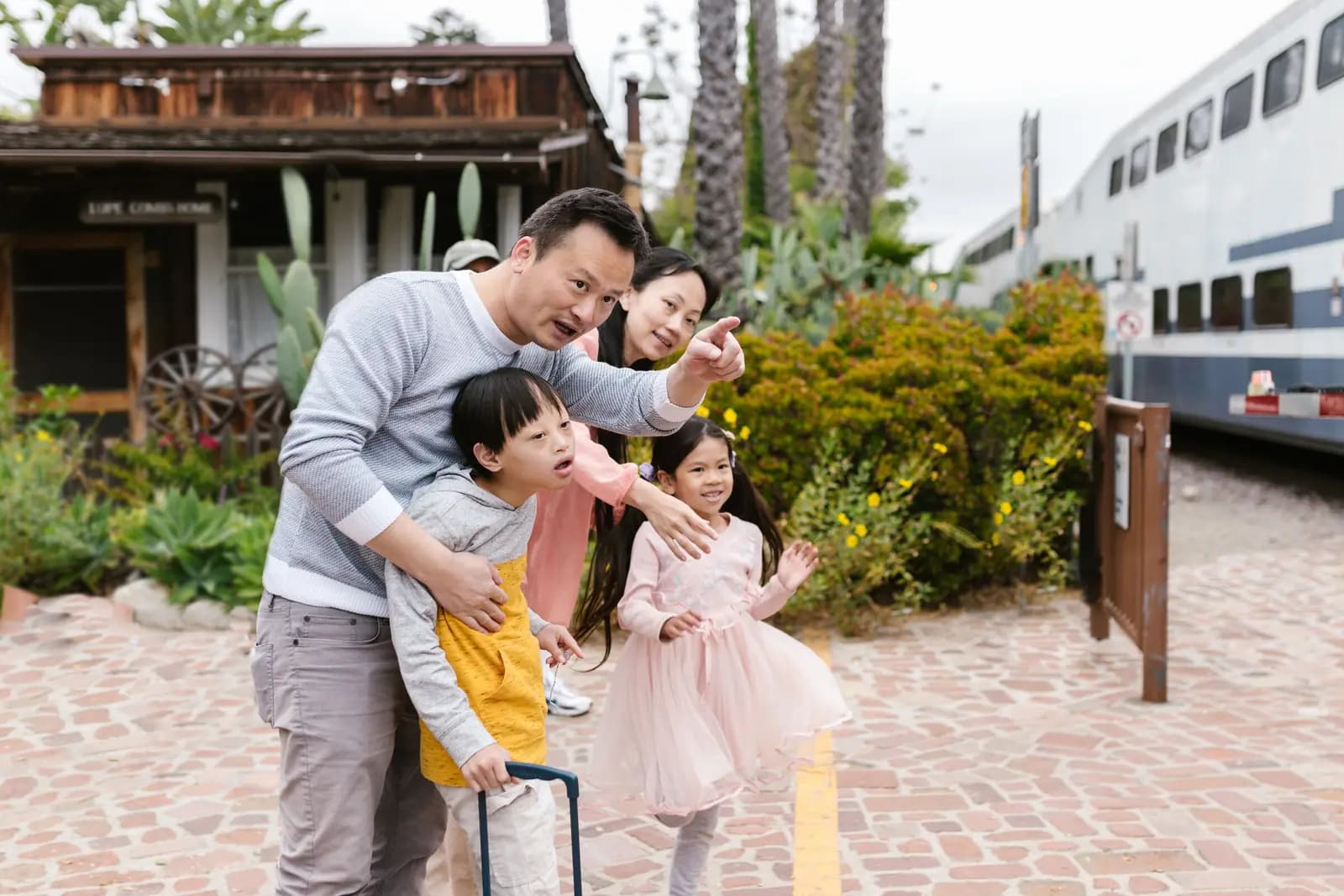 A father, a mother and two children stand on a paved path beside a train, the father and the children pointing at something off to the side.