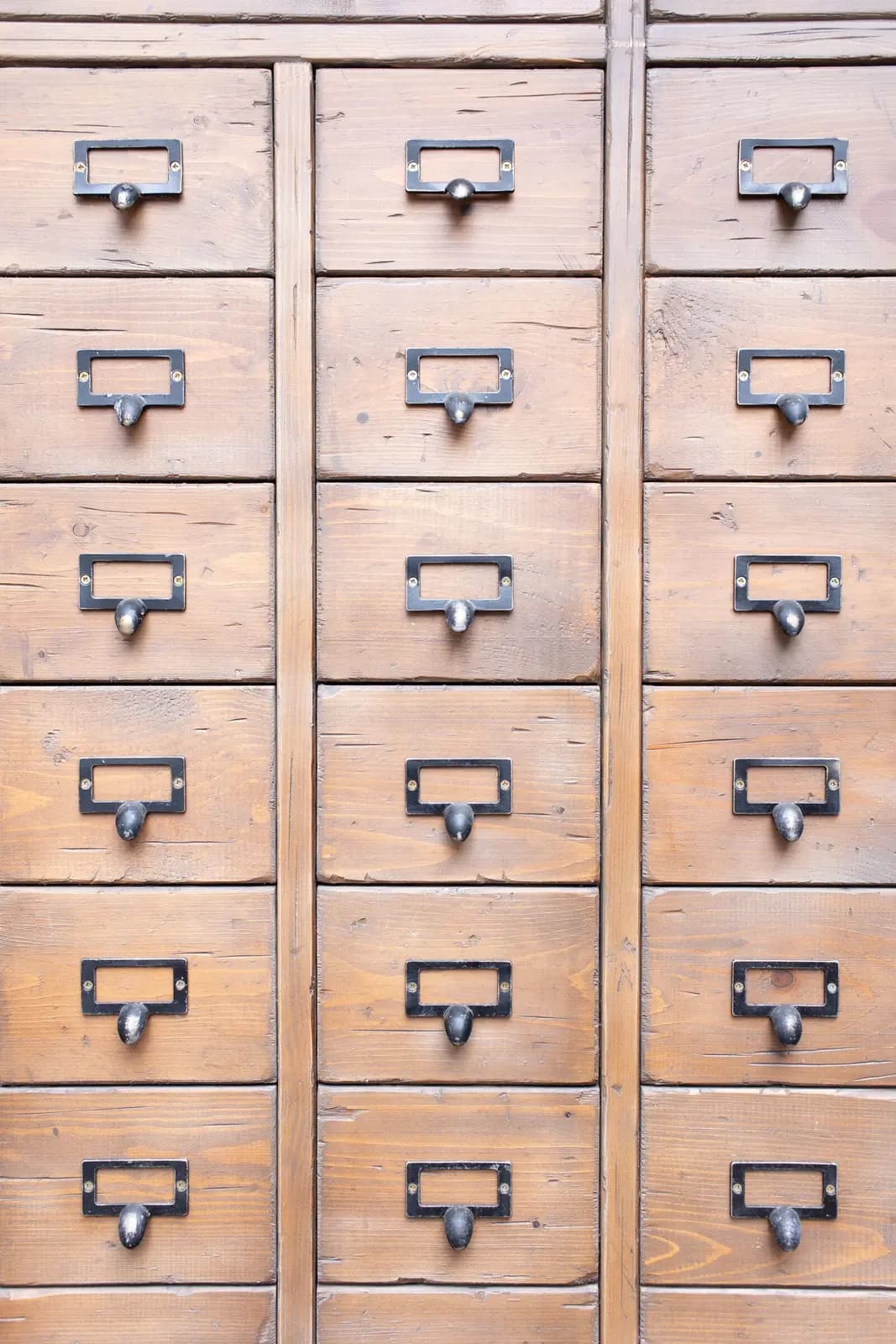 A wooden card-catalog cabinet with a metal label holder on every drawer.