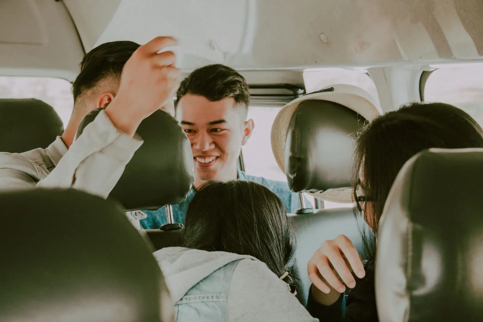 Friends in a car laugh together on a road trip, a passenger turned around to talk to the back seat.