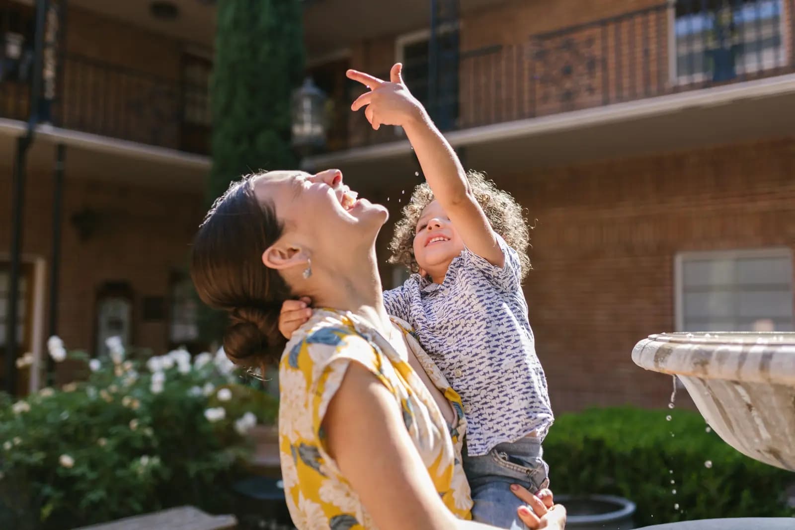 A mother holds her small son as they look up, the boy pointing at an old brick building with iron balconies.