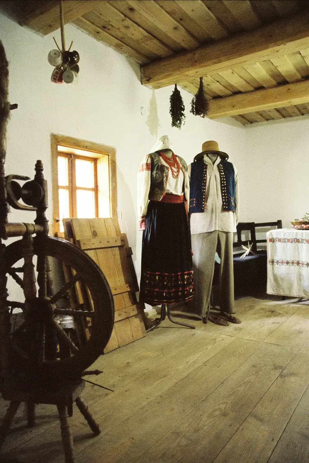 A period room with a spinning wheel in the foreground and costumes on mannequins.