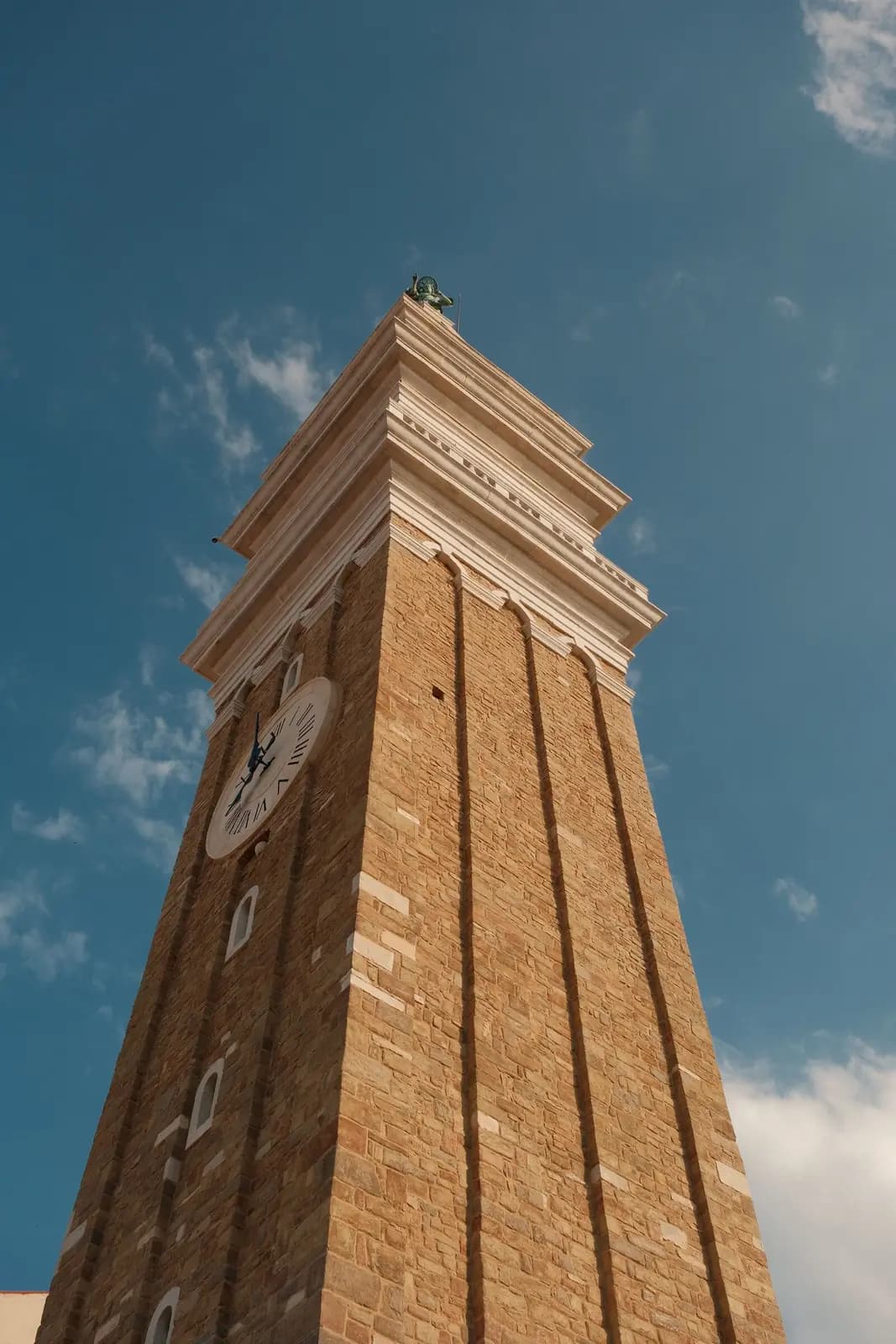 A brick clock tower seen from below against a blue sky.