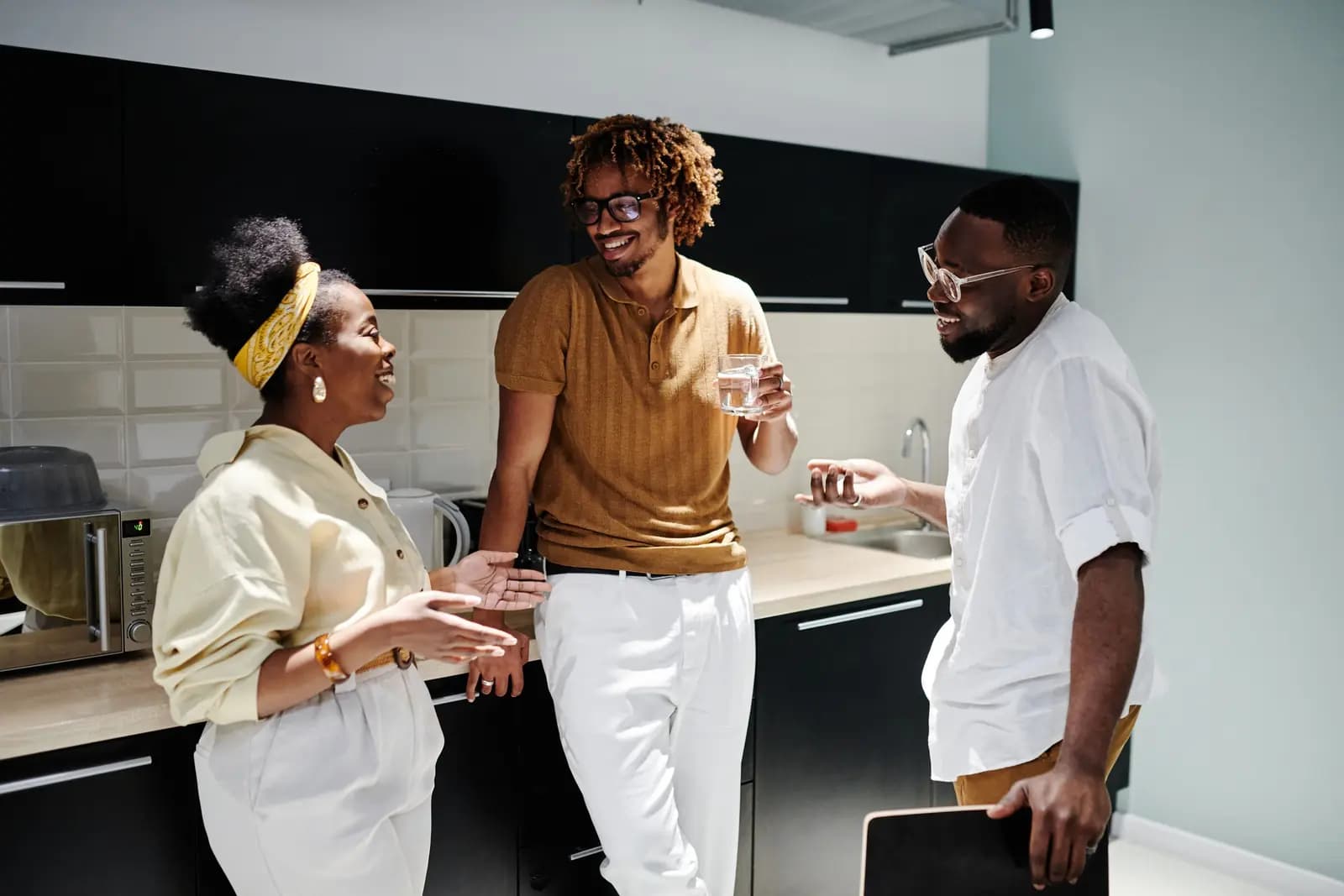 Three coworkers chat and laugh in a bright office kitchen.