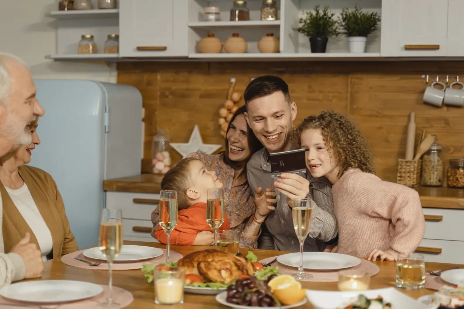 A family around a Thanksgiving table looks at a phone together, with grandparents seated beside them.