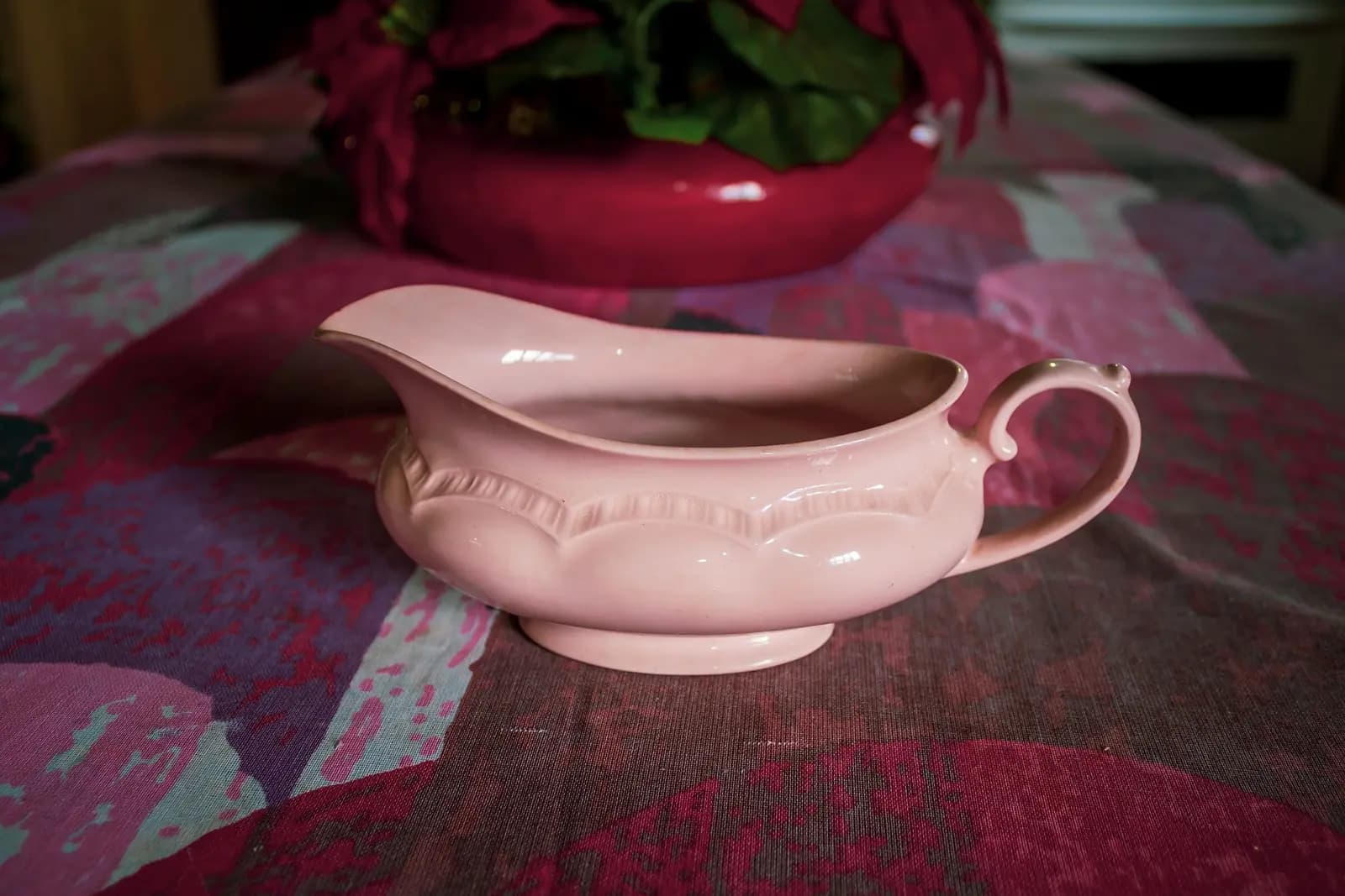 A pink gravy boat on a table with a patterned cloth.