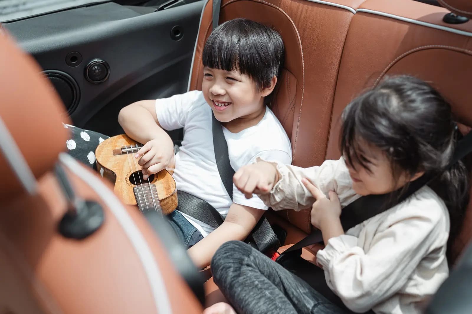 Two children laughing together in the back seat of a car.